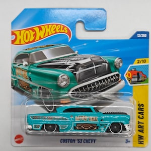 Peut inclure: Une voiture jouet moulée sous pression turquoise et noire, étiquetée "Custom '53 Chevy" sur une carte Hot Wheels bleue et jaune. La voiture présente un design détaillé avec les mots "Hot Wheels" dans une police en forme de flamme. La voiture fait partie de la série HW Art Cars.