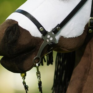 Puede incluir: Primer plano de una cabeza de caballo de peluche marr&oacute;n y blanco con una brida de cuero negro y una boquilla de plata. El caballo tiene una crin y una cola negras.