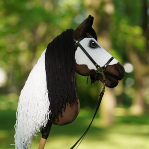 Puede incluir: Un caballo de madera marr&oacute;n y blanco con una crin y cola de lana negra. El caballo lleva una brida de cuero negro con una hebilla plateada.