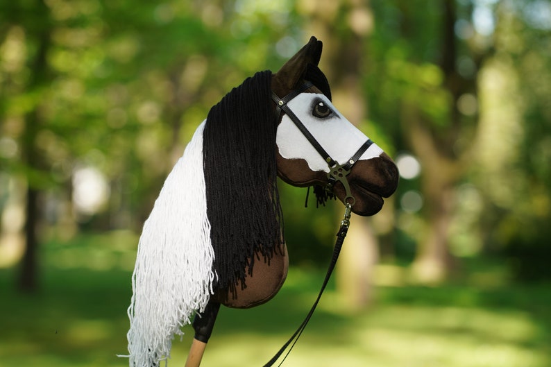 Puede incluir: Un caballo de madera marr&oacute;n y blanco con una crin y cola de lana negra. El caballo lleva una brida de cuero negro con una hebilla plateada.