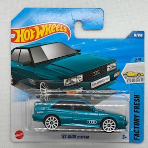 May include: A teal Hot Wheels die-cast model of an '87 Audi Quattro. The car has white wheels and the Audi logo. The packaging includes the Hot Wheels logo and the text "FACTORY FRESH".
