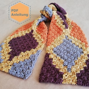Puede incluir: Una bufanda de ganchillo con un patrón geométrico en tonos naranja, amarillo, azul y marrón. La bufanda está anudada y el texto "PDF Anleitung" es visible en la esquina superior izquierda.