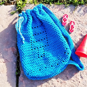 Könnte beinhalten: Eine hellblaue gehäkelte Kordeltasche mit weißem Besatz. Die Tasche liegt auf einer Steinoberfläche mit roten Flip-Flops und einem roten Kegel daneben.
