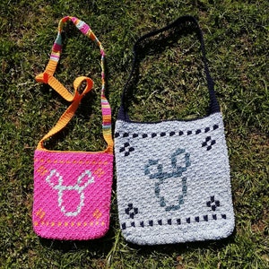 Könnte beinhalten: Zwei gehäkelte Taschen mit bunten Trägern. Die kleinere Tasche ist pink mit einem weißen Hirsch-Design. Die größere Tasche ist hellblau mit einem dunkelblauen geometrischen Design.