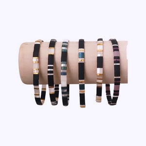 May include: A set of six colorful bracelets with black and white stripes and gold accents. The bracelets are made of small, square tiles and are stacked on a wooden surface.