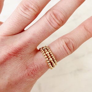 May include: Three gold beaded rings stacked on a finger. The rings are made of small, round beads.