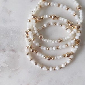 May include: A set of five bracelets with white shell beads and gold beads.