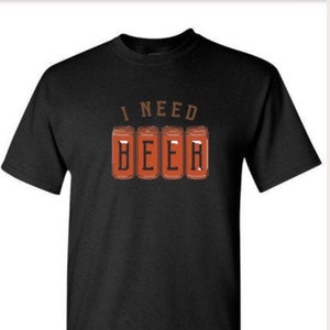 May include: Black t-shirt with the text "I NEED BEER" in brown letters above four orange beer can illustrations. The shirt is a short-sleeved crew neck.