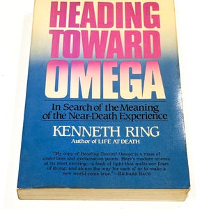 May include: A hardcover book titled "HEADING TOWARD OMEGA" with a gradient cover of pink, yellow, and blue. The author's name, Kenneth Ring, is displayed prominently. The book explores the meaning of near-death experiences.