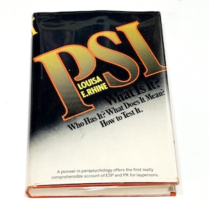 May include: A vintage book titled "PSI" with a black cover and orange lettering. The book's title is prominently displayed, along with the author's name, Louisa E. Rhine, and the questions "What Is It?" and "Who Has It?" The book has a white and orange gradient background.