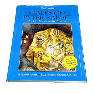 May include: A hardcover book titled "The Complete Tales of Peter Rabbit and Other Favorite Stories." The cover features a blue border and an illustration of rabbits in a cozy setting. The book is by Beatrix Potter and illustrated by Charles Santore.