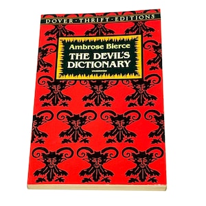 May include: A paperback book titled "THE DEVIL'S DICTIONARY" by Ambrose Bierce. The cover is red with a repeating black devil face pattern. The title is in large, bold, black letters with a yellow and green border.