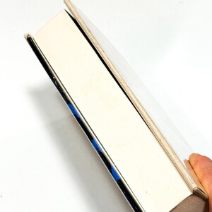 A hand is holding a book with a white spine and a blue spine, against a white background.