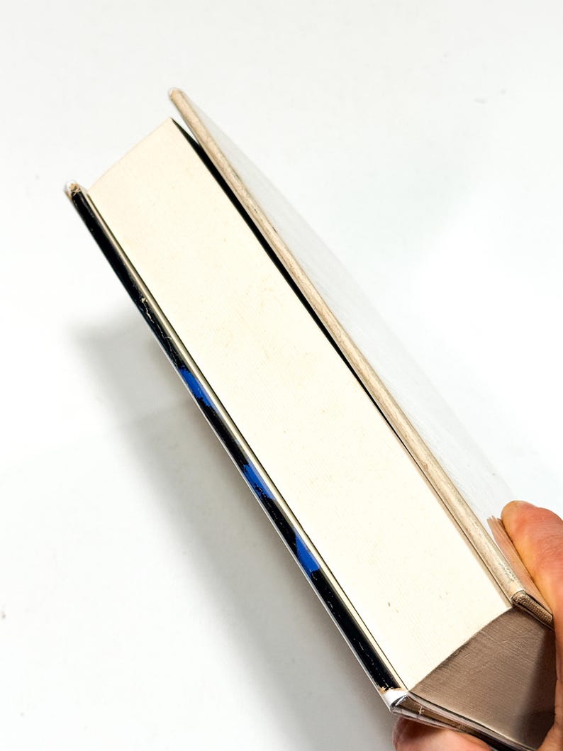 A hand is holding a book with a white spine and a blue spine, against a white background.