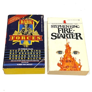 May include: Two vintage paperback books. The first, "Dark Forces," has a dark blue cover with a grim reaper graphic. The second, "Firestarter," features a flame design with eyes. Both books are by Stephen King.