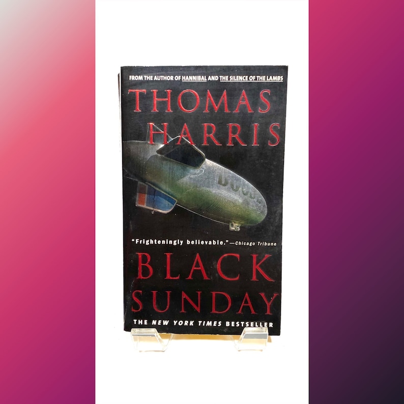 Pu&ograve; includere: Una copertina di un libro tascabile con sfondo nero e un dirigibile argentato. Il titolo &egrave; "Black Sunday" di Thomas Harris. Il libro &egrave; un best-seller del New York Times.