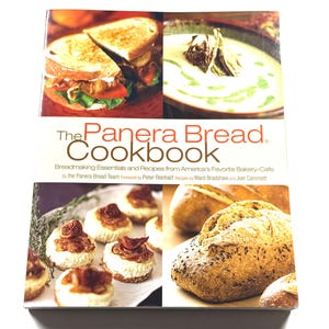 May include: The Panera Bread Cookbook. The cover features images of sandwiches, soup, bread, and pastries. The title is in red and brown, with the subtitle "Breadmaking Essentials and Recipes from America's Favorite Bakery-Cafe."