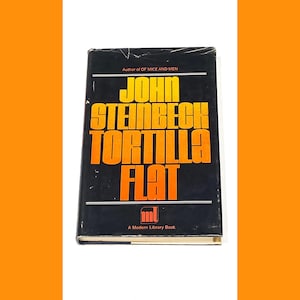 Puede incluir: Un libro de bolsillo negro y naranja con el título "Tortilla Flat" de John Steinbeck. El libro es un libro de la Modern Library.