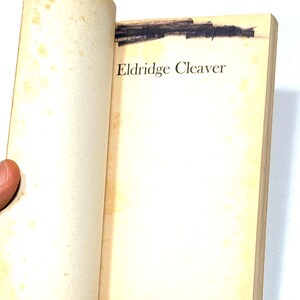 May include: Open book with yellowed pages. The title "Eldridge Cleaver" is printed in black on the right page. A dark, blacked-out area is visible at the top of the pages. The book's pages are slightly curved.