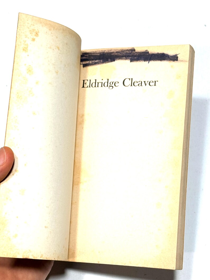 May include: Open book with yellowed pages. The title "Eldridge Cleaver" is printed in black on the right page. A dark, blacked-out area is visible at the top of the pages. The book's pages are slightly curved.