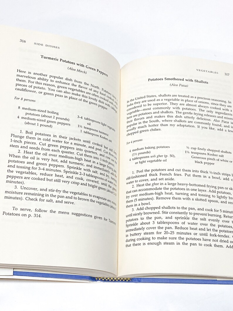May include: A vintage cookbook page with two recipes for side dishes: Turmeric Potatoes with Green Peppers and Potatoes Smothered with Shallots. The recipes include ingredients, instructions, and serving suggestions.
