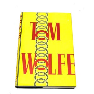 May include: A hardcover book with a bright yellow cover. The title "TOM WOLFE" is printed in large red letters. A series of interlocking circles runs vertically down the center of the cover. The book's spine is visible on the left side.