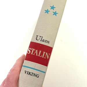 Puede incluir: Lomo de libro con el t&iacute;tulo "STALIN" en blanco sobre fondo rojo. El nombre del autor, "Ulam", est&aacute; encima, y la editorial, "VIKING", debajo. Tres estrellas turquesas est&aacute;n impresas en la parte superior.