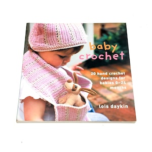 May include: A book titled "baby crochet" with a baby wearing a pink crocheted hat and scarf. The book cover features the text "20 hand crochet designs for babies 0-24 months" and the author's name, Lois Daykin.