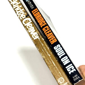 May include: Two vintage paperback books. One book has a gold cover with the name "Eldridge Cleaver" in white. The other book has a black cover with the title "Soul on Ice" and the author's name in orange.
