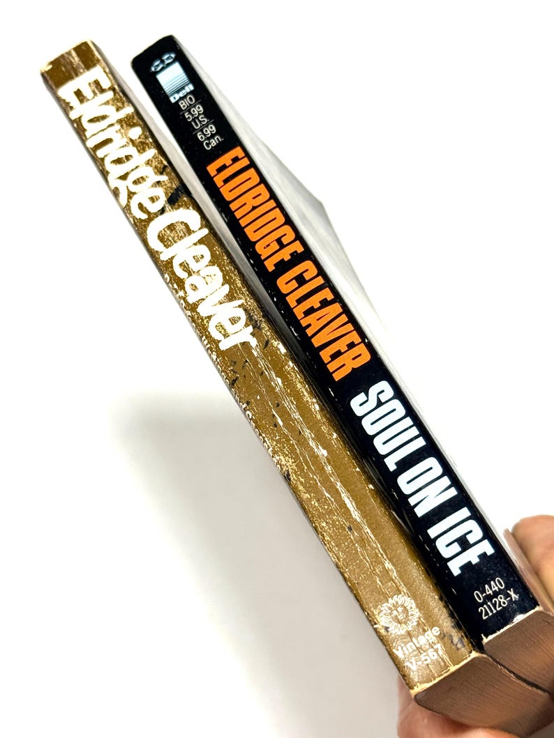 May include: Two vintage paperback books. One book has a gold cover with the name "Eldridge Cleaver" in white. The other book has a black cover with the title "Soul on Ice" and the author's name in orange.
