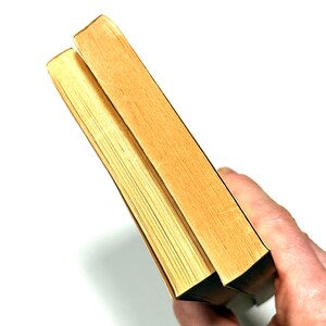 May include: Two hardcover books with light brown pages and edges are held against a white background. The covers are a light tan color. The books are slightly angled, showing the pages and the spine.