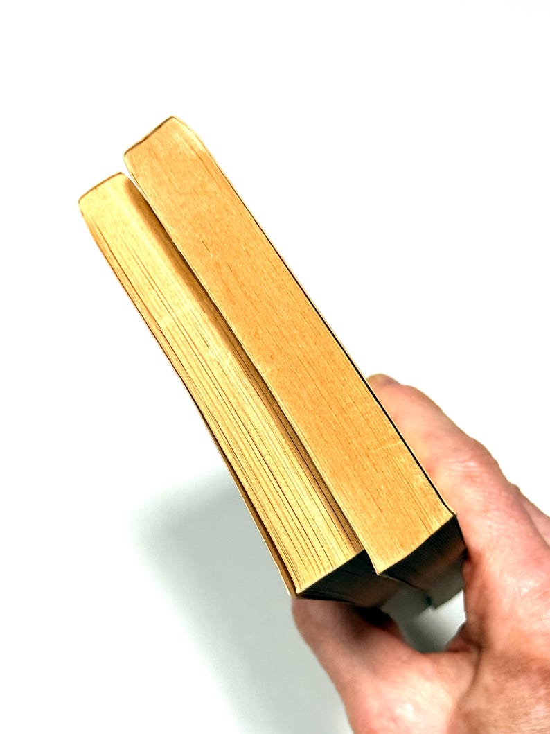 May include: Two hardcover books with light brown pages and edges are held against a white background. The covers are a light tan color. The books are slightly angled, showing the pages and the spine.
