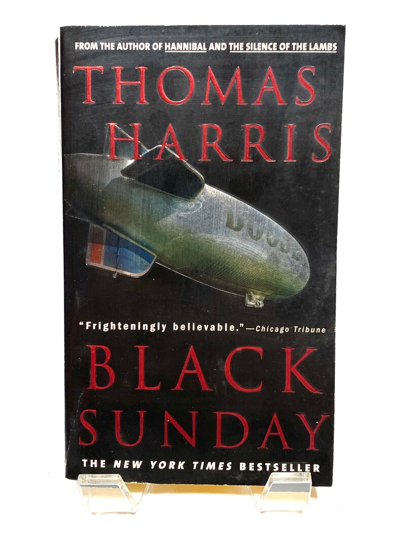 Pu&ograve; includere: Una copertina di un libro tascabile con sfondo nero e titolo rosso. Il titolo &egrave; "BLACK SUNDAY" di Thomas Harris. La copertina presenta un dirigibile con le parole "U.S." sul lato. Il testo "From the author of Hannibal and The Silence of the Lambs" &egrave; in cima alla copertina. Il testo "The New York Times Bestseller" &egrave; in fondo alla copertina.