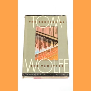 May include: A book cover with a gray background and the title "The Bonfire of the Vanities" by Tom Wolfe. The cover features a cityscape reflected in a glass table.