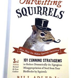 May include: A book titled Outwitting Squirrels by Bill Adler Jr. The cover features a squirrel wearing a black top hat and a black mustache. Text includes 3rd Edition Revised & Even Craftier, 101 Cunning Stratagems to Reduce Dramatically the Egregious Misappropriation of Seed from Your Birdfeeder by Squirrels, and More Than One Million Squirrels Outwitted.
