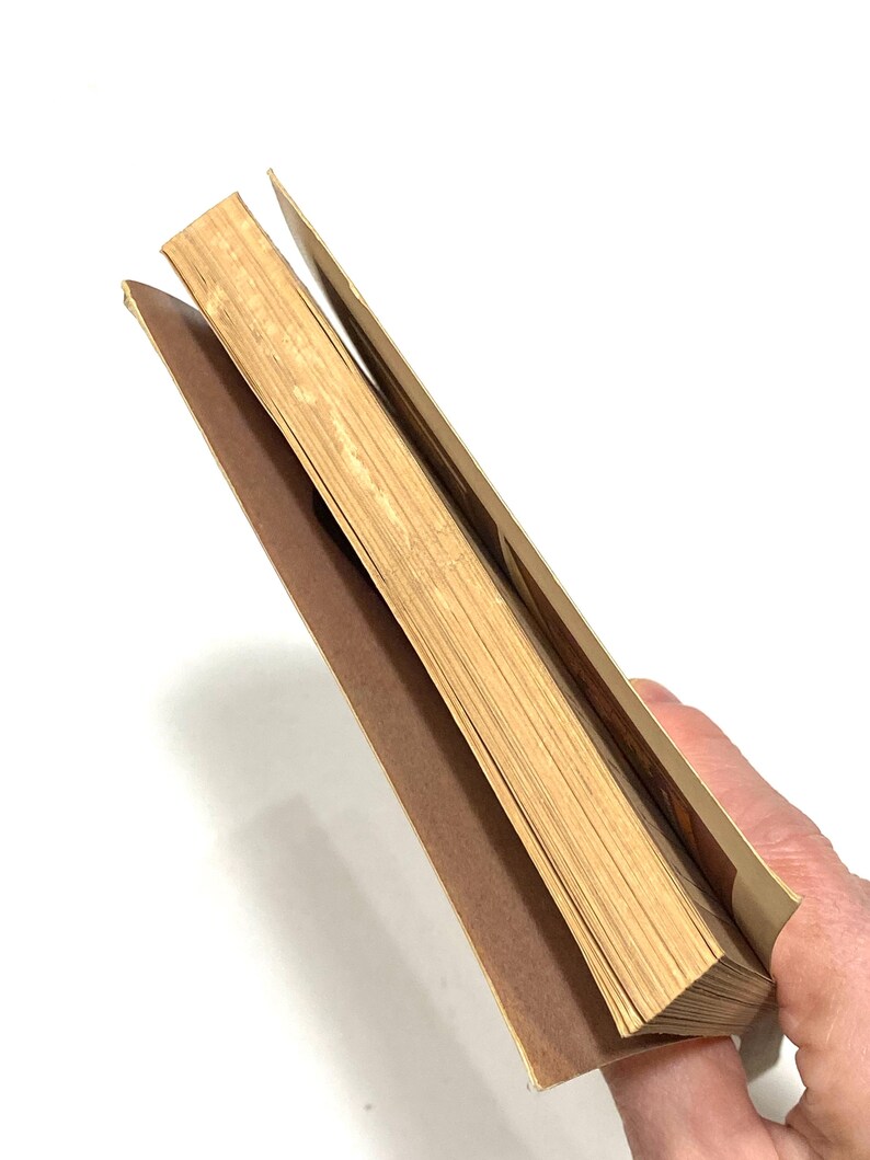 A hand is holding a stack of brown paper or cardboard, with the pages of the book visible.