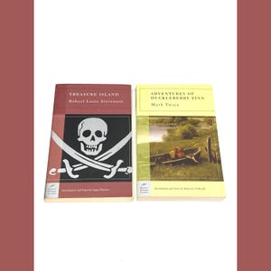 May include: Two classic books are displayed side-by-side. "Treasure Island" by Robert Louis Stevenson features a skull and crossbones on the cover. "Adventures of Huckleberry Finn" by Mark Twain has a landscape scene.