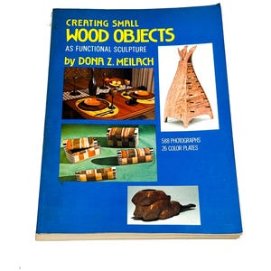 May include: A softcover book titled Creating Small Wood Objects as Functional Sculpture by Dona Z. Meilach. The blue cover features three photographic insets displaying various wooden items, including boxes, a tall sculpture, and a pipe.