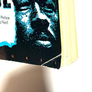 May include: A book with a black cover featuring a blue and white image of a face. The title is partially visible, with the letters "UREL" at the bottom. The book's pages are yellowed.