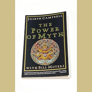 May include: A black book with gold lettering titled "The Power of Myth" by Joseph Campbell with Bill Moyers. The book cover features a colorful illustration of a dragon.