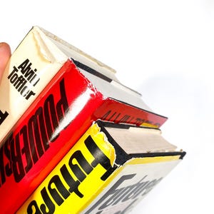 a hand holding a stack of books in front of a white background