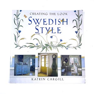 May include: A hardcover book titled Creating the Look Swedish Style by Katrin Cargill. The white cover features a floral illustration with wheat stalks and butterflies, plus three inset photos of interior rooms and furniture.