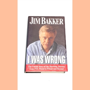 May include: A book titled "I Was Wrong: The Untold Story of the Shocking Journey from PTL Power to Prison and Beyond" by Jim Bakker. The cover features a photo of Jim Bakker, a white man with short gray hair, wearing a blue shirt.
