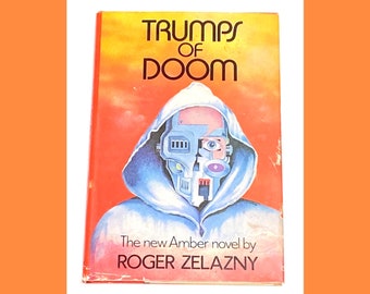 May include: A book cover with a red background and a blue hooded figure with a robotic face. The title of the book is "Trumps of Doom" and the author is "Roger Zelazny".
