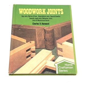 May include: A green book titled "WOODWORK JOINTS" with text about edge joints, mortise & tenon, and other woodworking techniques. The author's name is Charles H. Hayward. The cover features images of various wood joints. The book is part of the "Home Craftsman Series."