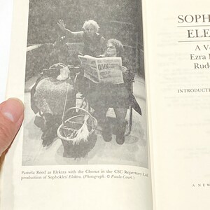 以下が含まれることがあります： 車椅子に座った女性が膝の上に新聞を持っている白黒写真。女性は長袖のシャツと帽子をかぶっています。この写真は、ソフォクレスのエレクトラの演劇作品からのものです。