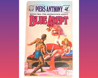 May include: A paperback book cover with a fantasy illustration of a man and woman in a room with a red couch. The book title is "Blue Adept" and the author is Piers Anthony. The book is part of a series called "The Apprentice Adept".