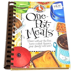 May include: A spiral-bound cookbook titled "One-Pot Meals" with illustrations of various dishes. The cover features a red pot lid, a blue pot, and a price tag. The text reads "Flavor without the fuss... home-cooked dinners your family will love!"