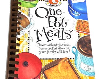 May include: A spiral-bound cookbook titled "One-Pot Meals" with illustrations of various dishes. The cover features a red pot lid, a blue pot, and a price tag. The text reads "Flavor without the fuss... home-cooked dinners your family will love!"