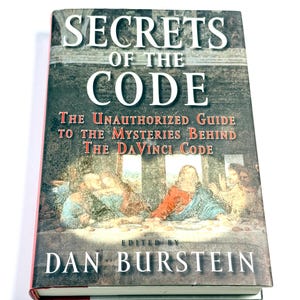 May include: A hardcover book titled Secrets of the Code: The Unauthorized Guide to the Mysteries Behind The DaVinci Code, edited by Dan Burstein. The cover features a reproduction of The Last Supper painting with white and red text.